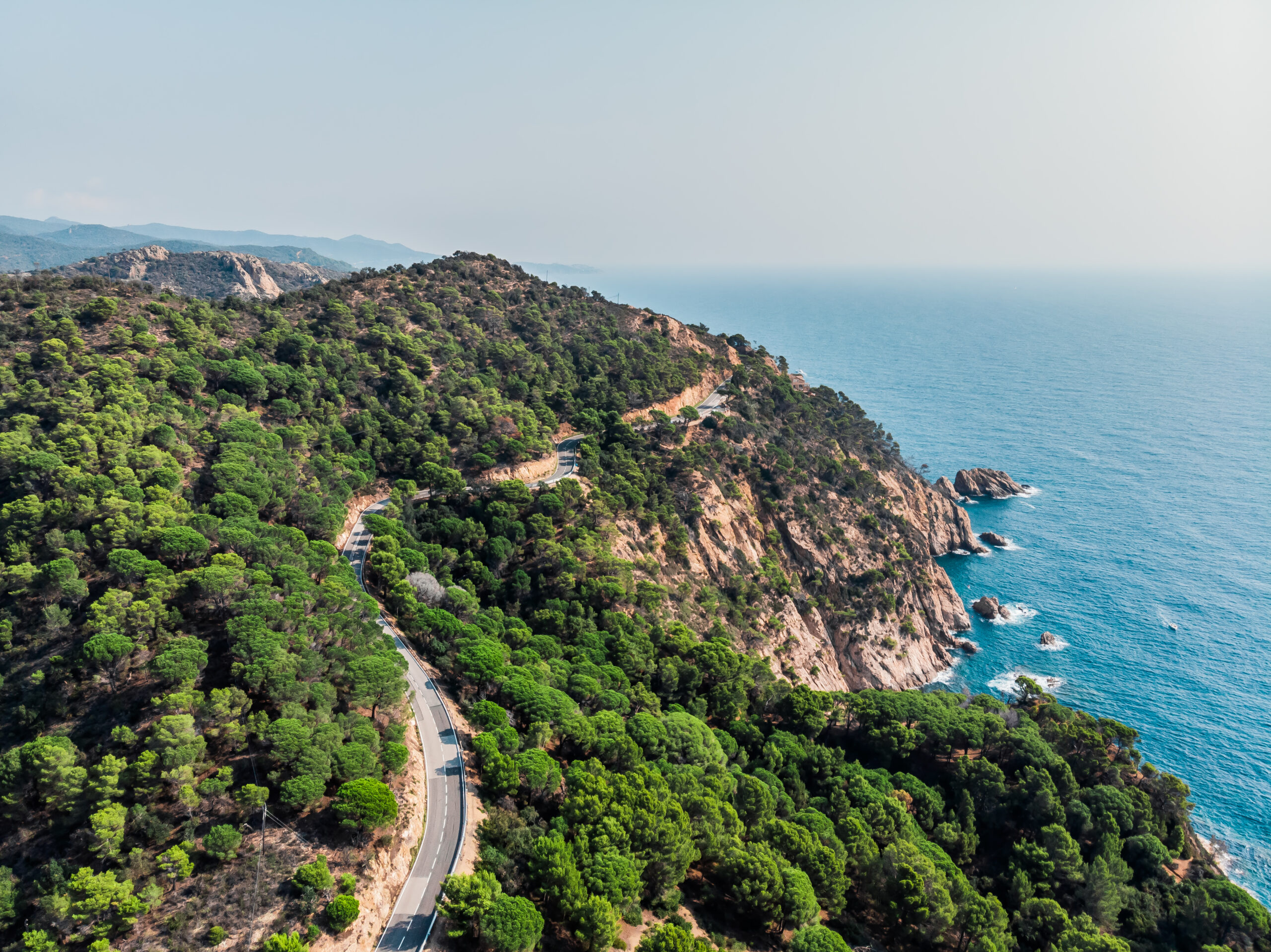 View from a drone on a mountain serpentine in the city of Tossa de Mar. Drone shot of a car driving along a mountain road. The resort town of Tossa de Mar near the Mediterranean Sea.