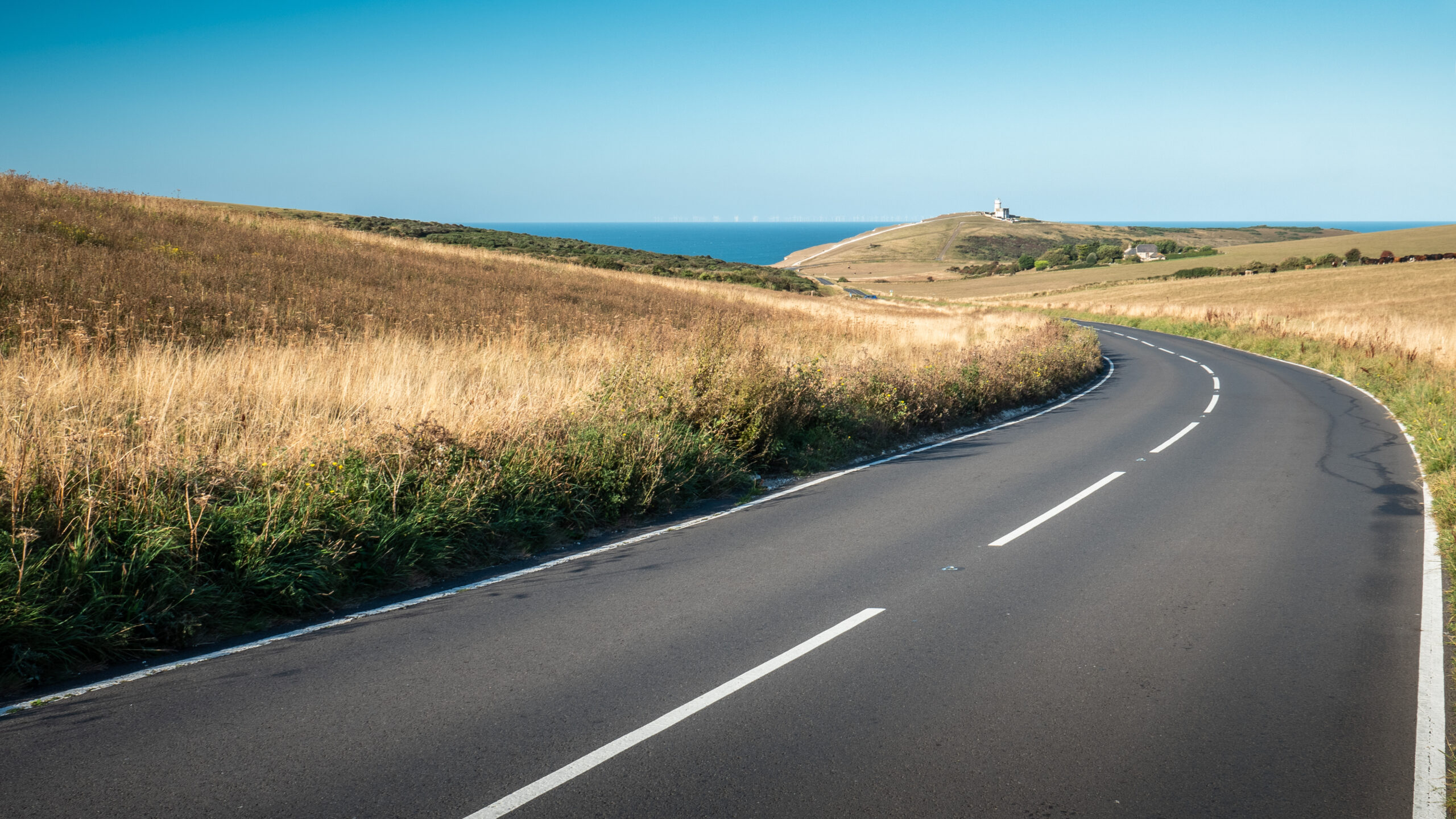 The South Downs and Belle Tout lighthouse, Sussex, England. A curved road leading to the English Channel coastline with Belle Tout lighthouse visible.